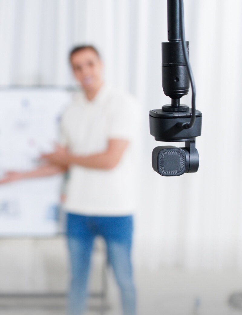 OBSBOT Tiny SE — mounted upside down on a pole in front of a presenter
