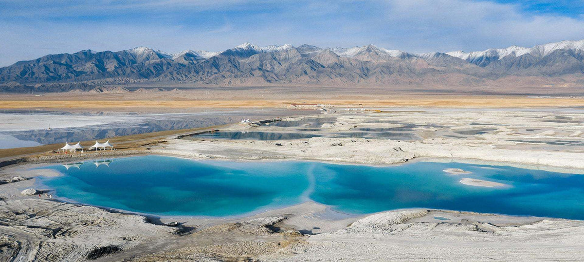 Salt flats with turquoise pools and distant mountains under a clear blue sky.