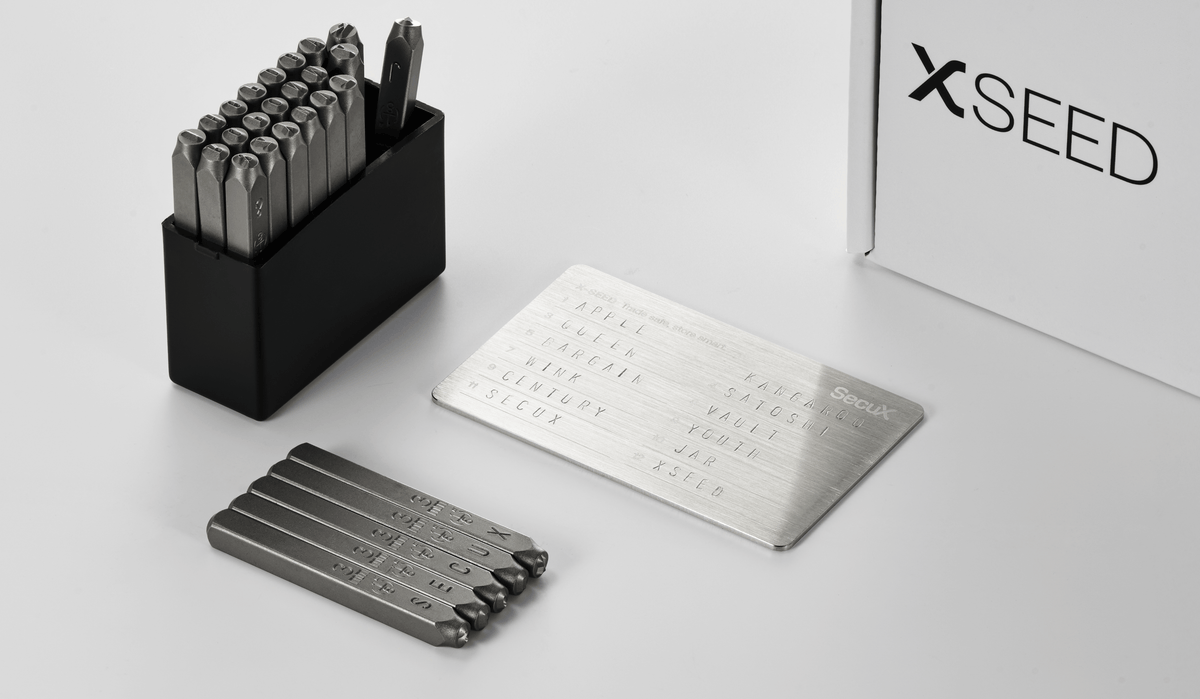 SecuX X-SEED Plus steel letter punches beside a stainless steel plate stamped with twelve recovery words
